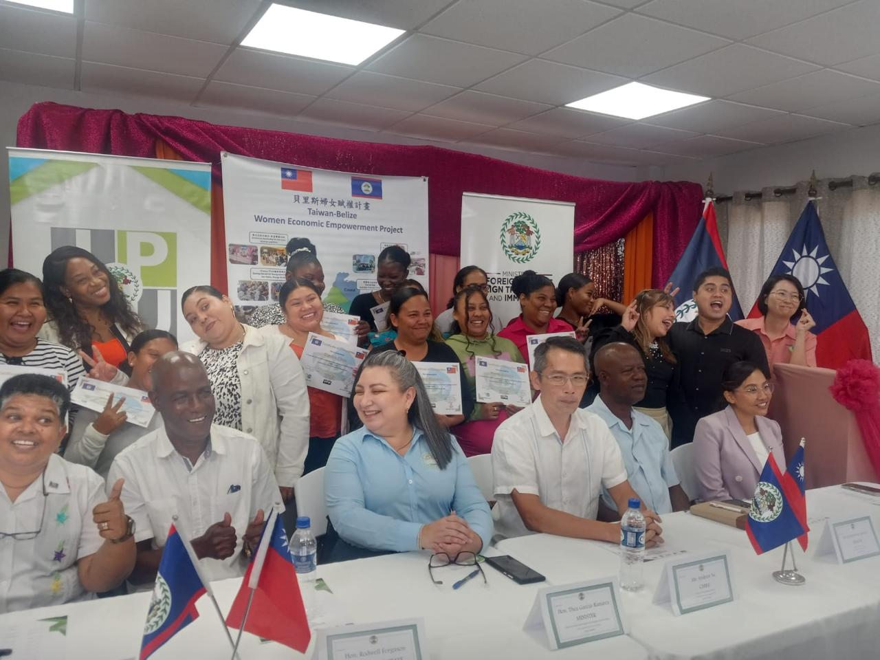 Graduates holding their certificates with guests and the Belize and Taiwan flags